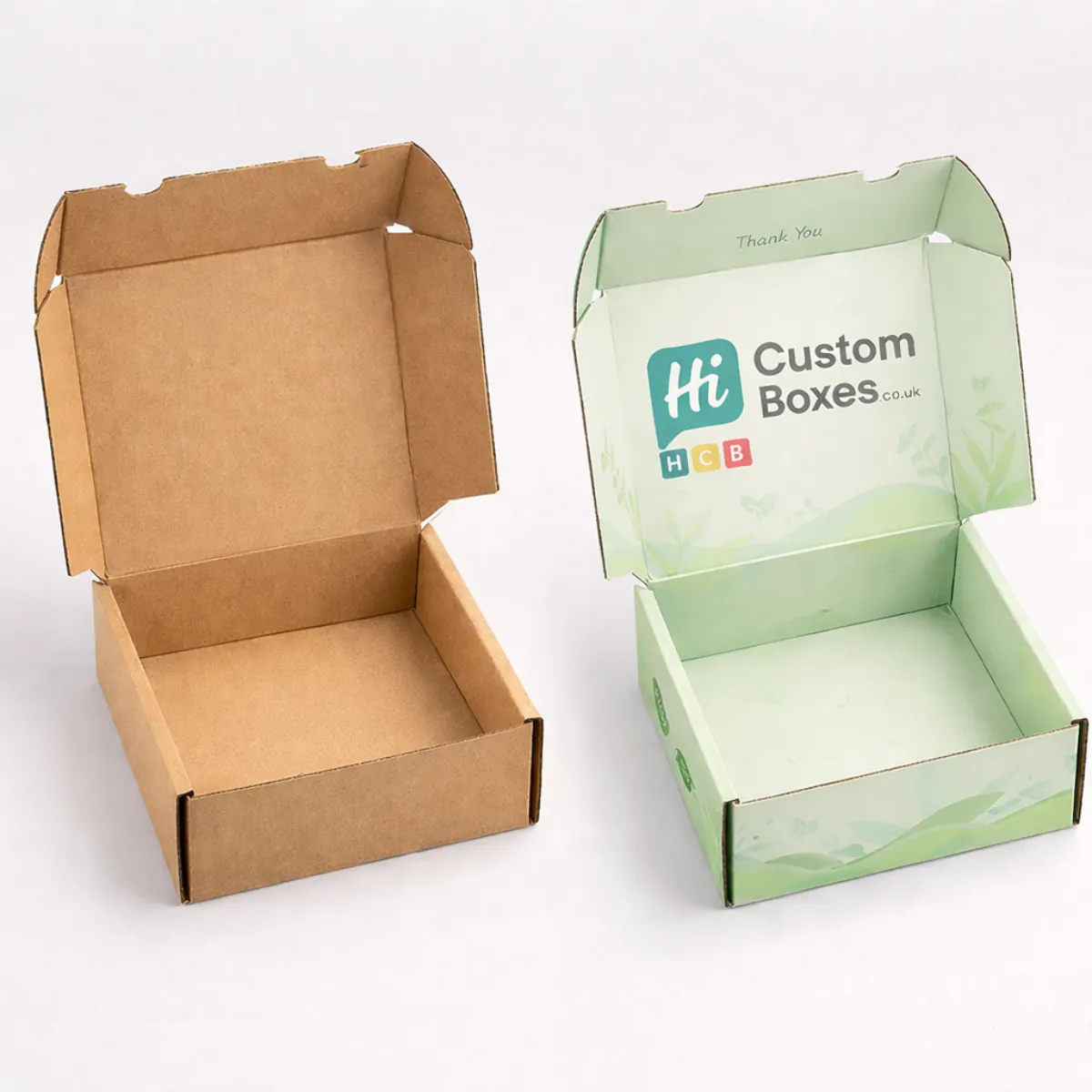 Two small, open square mailer boxes: one natural brown kraft and one printed with green leaves. class=